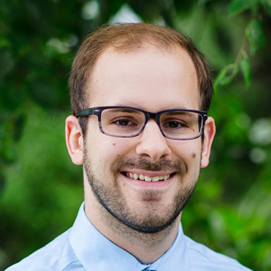 man with glasses smiling, green foliage background